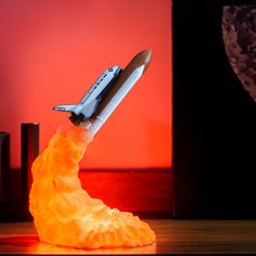 a toy rocket ship on top of an orange flame with a red light in the background