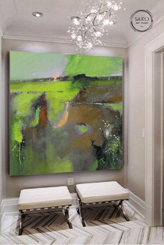 a large painting hanging on the wall in a room with two stools and a chandelier