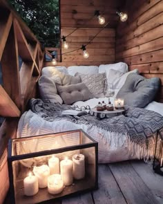 a bed sitting on top of a wooden floor covered in pillows and blankets next to lit candles