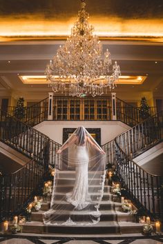 the bride is walking down the stairs in her wedding dress with veil flowing over her head