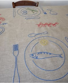 the table cloth has blue thread on it and is decorated with images of fish, food, and other things