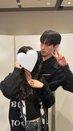 a man and woman standing next to each other in front of a mirror holding up a heart