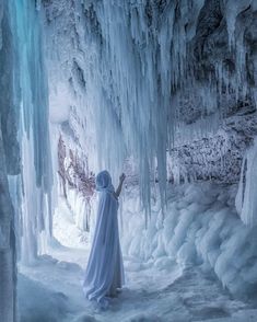 a woman dressed in white is standing inside an ice cave with icicles on the walls