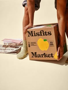 a person is holding a box that says misfits market on it and there's a pair of shoes next to it