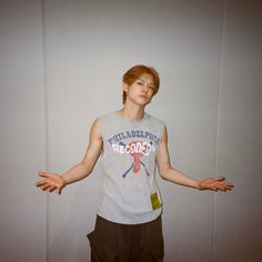 a young man standing in front of a white wall with his hands out to the side