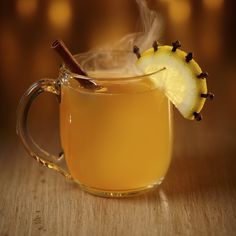 a glass mug filled with liquid and topped with an apple slice, cinnamon stick and vanilla