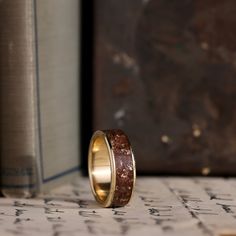 a gold wedding band with red and white speckles sits on top of an old book