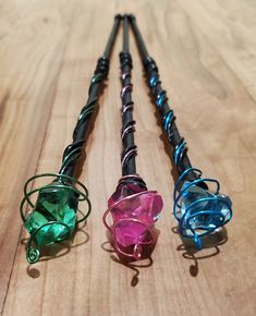 four different colored glass objects on a wooden surface with wire wrapped around them and attached to the handles