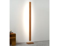 a wooden floor lamp in front of a white wall with a light on it's side