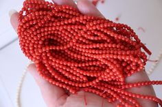 a hand holding a string of red beads on a white surface with other beads in the background