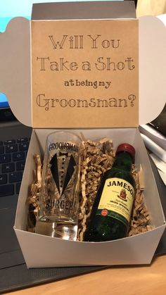 an open box containing alcohol and liquor on a desk next to a laptop computer, which reads will you take a shot at being my groomsman?