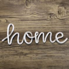 the word home written in white yarn on a wooden surface