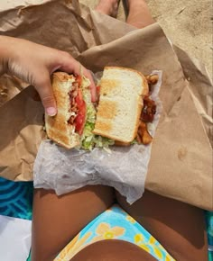 a close up of a person holding a sandwich in their hand and laying on the beach