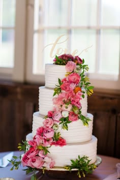 a three tiered cake with pink flowers on the top is sitting on a table