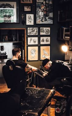 two men sitting in chairs with tattoos on their arms and one has his arm wrapped around another man's shoulder