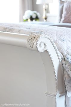 a white bed with floral bedspread and pillows on it's headboard