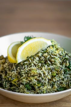 a white bowl filled with green and yellow food next to a slice of lemon on top of a wooden table