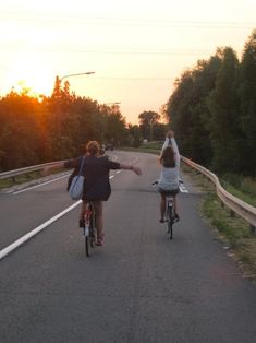 two people riding bikes on a road with the sun setting in the distance behind them