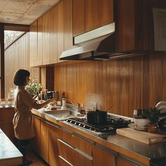 a woman standing in a kitchen next to a stove top oven under a hood with pots and pans on it