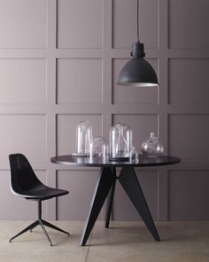 a dining table with two chairs and a glass vase on it in front of a gray wall