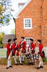 a group of men in red uniforms playing drums and drums outside a brick building with a white picket fence