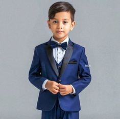 a young boy in a blue suit and bow tie posing for the camera with his hands on his hips