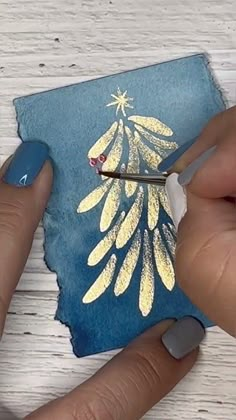 someone using scissors to paint a christmas tree on a piece of blue paper with gold foil