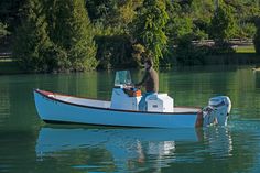 a man riding on the back of a white boat in a lake next to trees