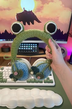 a person is holding up a frog earbuds in front of a computer screen