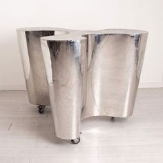 two silver metal tables sitting on top of a white tile floor next to each other