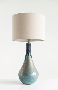 a blue vase with a white shade on it sitting next to a light that is turned on