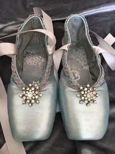 a pair of baby blue shoes with pearls and bows on the bottom, sitting on a black blanket