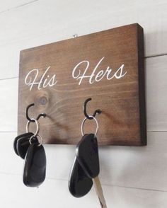 a pair of black earrings hanging from a hook on a wooden sign that reads, his herss