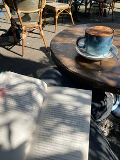 an open book sitting on top of a table next to a cup of coffee