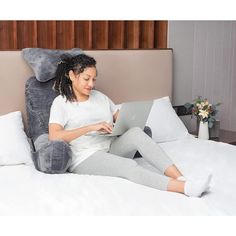 a woman sitting on a bed using a laptop computer with an elephant pillow behind her