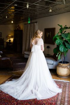 a woman in a wedding dress standing on a rug looking at the back of her gown