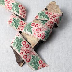 a roll of christmas ribbon with holly and red berries on white fabric next to a piece of wood