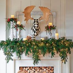 a mantel decorated with candles, greenery and deer heads on top of it