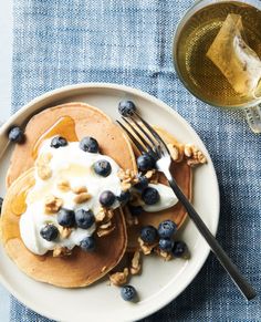 pancakes topped with blueberries and yogurt on a plate next to a glass of wine