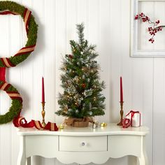 a small christmas tree sitting on top of a table next to a wreath and candles