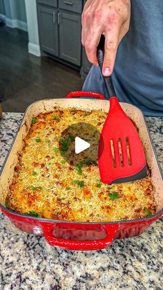 a red spatula is being used to mix up food in a casserole dish