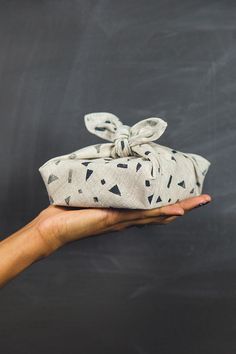 a hand is holding a small white bag with black and white designs on it, against a chalkboard background