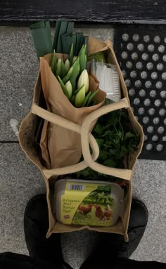 a bunch of flowers sitting in a bag on the ground next to a person's feet