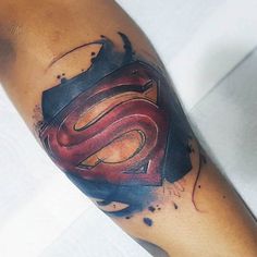 a man's arm with a superman symbol tattoo on it and watercolor splashes