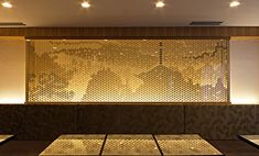 an empty restaurant with wooden tables and gold patterned wall behind the counter top, along with lights