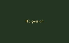 the words life goes on are written in gold ink against a dark green background with an oval border