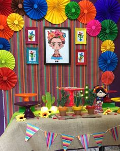 a table topped with lots of colorful paper fans next to a wall covered in pictures