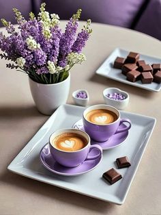 two cups of coffee on a plate with some chocolates and flowers in the background