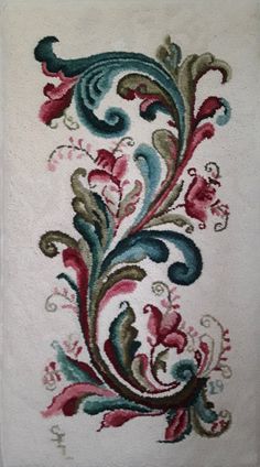 an embroidered wall hanging with flowers and leaves on white fabric, in the corner of a room