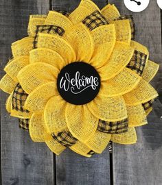 a yellow sunflower with the word welcome on it's center surrounded by black and white plaid fabric